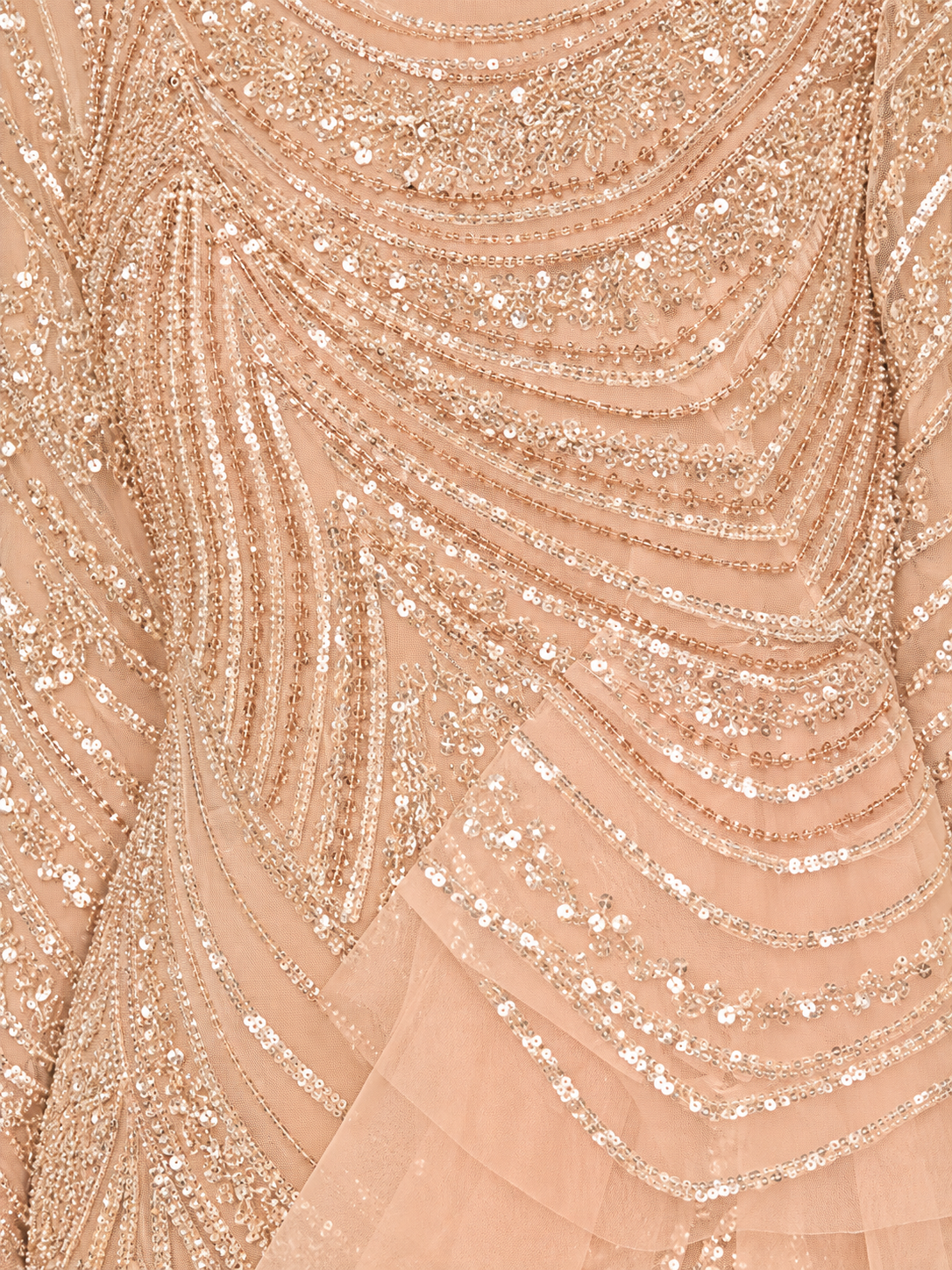 Close-up of a peach-beige embellished fabric with layered sequins and beadwork arranged in flowing curved lines.